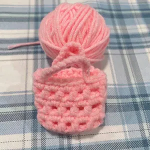 Nahaufnahme eines rosa handgehäkelten Mini-Taschenanhängers mit weichem Garnballen