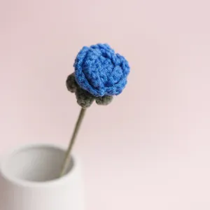 Wunderschöne handgestrickte blaue Häkelrose in einer eleganten weißen Keramikvase