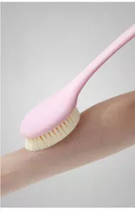 Close-up detail of a long handle pink bath brush scrubbing arm skin for effective exfoliation