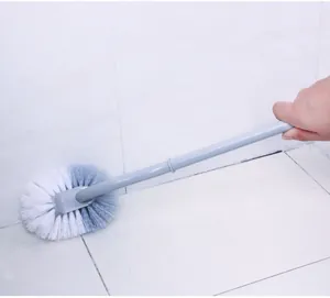 Detailed close-up of a grey long-handled toilet brush cleaning bathroom floor corners.