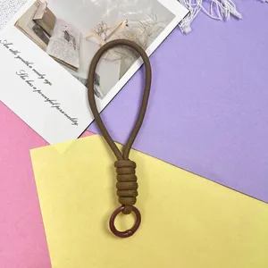 Detail van bruin gevlochten polsbandje met duurzame ring op kleurrijke basis.