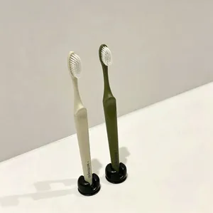 Close-up of minimalist toothbrushes in cream and olive green with black holders