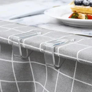 Transparent plastic tablecloth clips fixing a grey checkered cloth on dining table