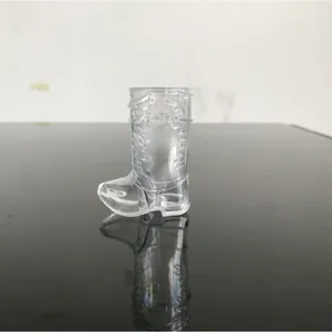 Transparent plastic cowboy boot shot glass shown on a dark reflective table surface.