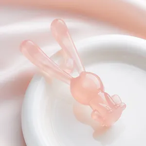 Masajeador facial con forma de conejo rosa y adorno decorativo colocado en un plato blanco