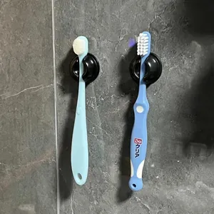Detail view of two wall-mounted black suction cup toothbrush holders on grey tile