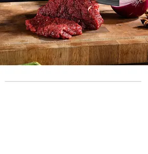 Detail view of a Damascus pattern kitchen knife slicing fresh raw meat on a wooden board