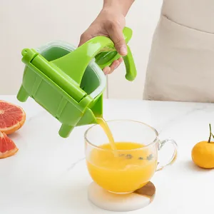 Handheld green plastic manual fruit juicer pouring fresh orange juice into a clear glass cup