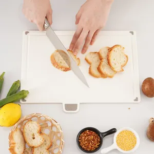 White plastic cutting board with non-slip corners being used to slice bread in a kitchen
