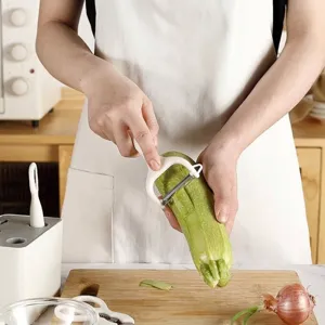 Ergonomischer weißer Küchenschäler aus Edelstahl schält eine frische grüne Zucchini