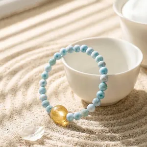 Natural blue Larimar and golden Lepidolite beaded bracelet displayed on Zen garden sand