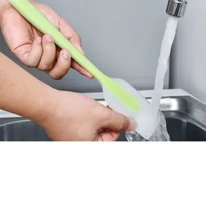 Gros plan d'une spatule en silicone verte rincée sous l'eau courante dans un évier