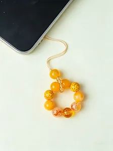 Detailopname van gele kristallen kralen telefoonbedel met gegraveerd rijkdomsteken erop