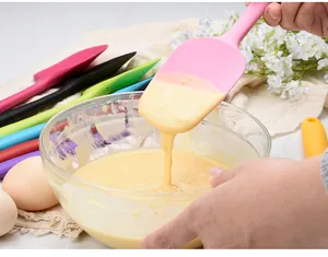 Gros plan d'une spatule en silicone rose mélangeant de la pâte à gâteau dans un bol