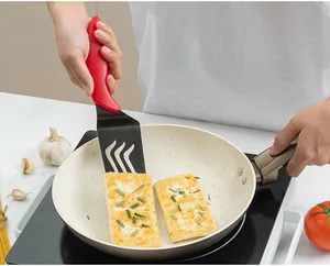 Dettaglio di una spatola con manico rosso che gira il cibo in una padella di ceramica