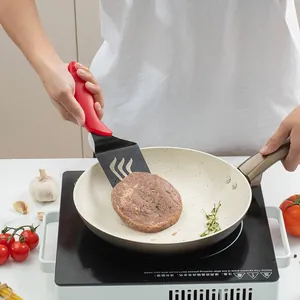 Spatola da cucina in acciaio inox con manico rosso mentre gira un hamburger in padella