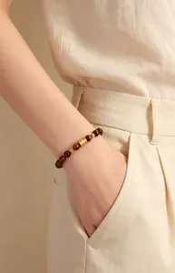 Nahaufnahme eines Armbands aus Tigerauge mit goldenem Filigran-Anhänger am Handgelenk.