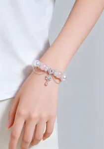 Primer plano de una pulsera de cuentas de cuarzo rosa y perlas con dije de mariposa en la muñeca.