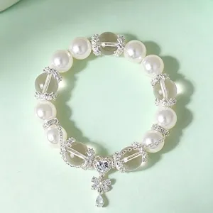 Elegante pulsera de perlas y cristal con dije de corazón y mariposa sobre fondo verde.