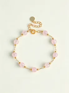 Detalle de una delicada pulsera de cuentas de cristal rosa con cadena dorada ajustable.