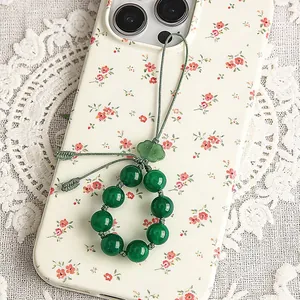 Nahaufnahme eines grünen Achat-Perlen-Handyanhängers mit vintage Blumenmuster-Hintergrund