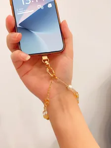 Close-up of a handmade yellow crystal and pearl phone strap attached to a smartphone.