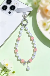Detailed view of pink and white cat's eye stone beaded phone strap on a green background