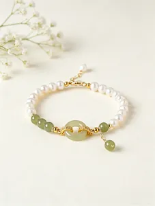 Detail view of a freshwater pearl and green jade bracelet with a golden safety buckle.