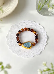 Detailed shot of a tiger eye bead bracelet featuring a blue gourd pendant in gold frame