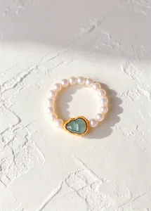 Close-up of elegant pearl ring with a green gourd-shaped gemstone in gold setting.