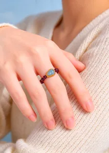 Detail shot of a garnet beaded ring with a light blue gourd gemstone on an Asian hand.