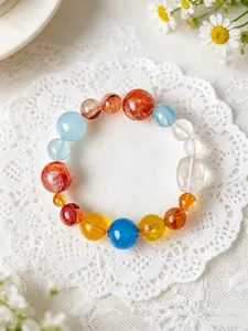 Draufsicht auf ein buntes Naturkristall-Armband auf weißer Spitze mit Gänseblümchen.