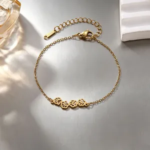 Primer plano de una pulsera de acero inoxidable dorada con dijes de huellas de gato caladas