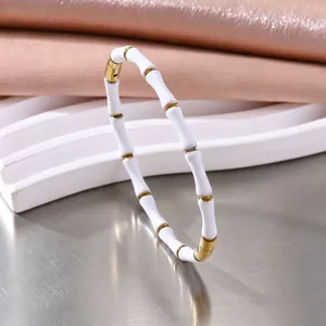 Detail van een wit geëmailleerde bamboe armband met goudkleurige roestvrijstalen accenten.
