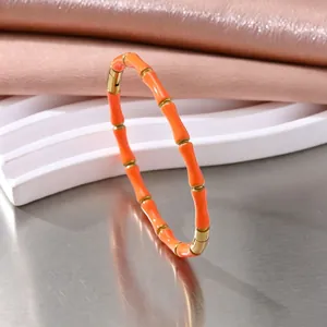 Detailopname van de oranje emaille bamboe-armband in goudkleurig roestvrij staal