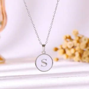 Vue détaillée d'un collier en acier inoxydable avec pendentif rond lettre S émail blanc.