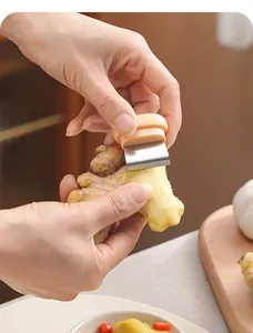 Detailed view of the handheld stainless steel tool peeling skin off a fresh ginger root
