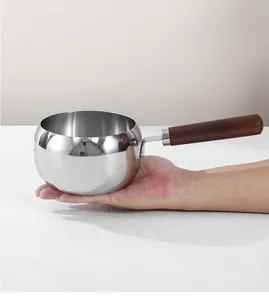 Kleine RVS melkpan met houten handvat in de hand gehouden om de grootte te tonen.