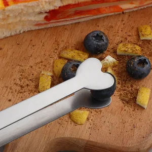 Heart-shaped stainless steel food tongs for sugar cubes and snacks on a wood board