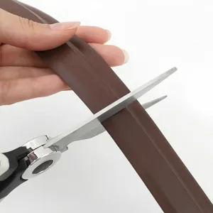 Brown self-adhesive door bottom seal strip being cut to custom length for weatherproofing