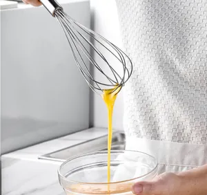 Detailed close-up view of stainless steel whisk mixing eggs in a clear glass bowl