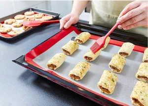Using red silicone pastry brush on baking rolls over a non-stick silicone mat