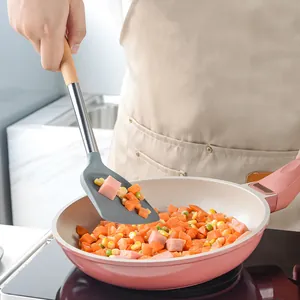 Grey silicone spatula with wooden handle used for cooking in a non-stick pan