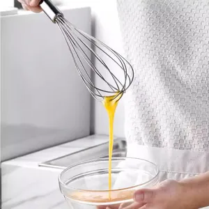 Professional stainless steel manual kitchen whisk beating fresh eggs in a clear glass bowl