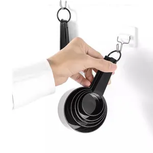 Set of black plastic measuring cups with handles hanging on a hook in the kitchen.