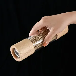 Manual oak and acrylic pepper grinder filled with peppercorns against a black background