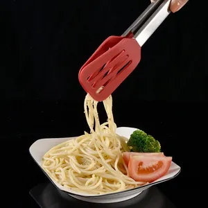 Red silicone and stainless steel kitchen tongs picking up spaghetti from a plate