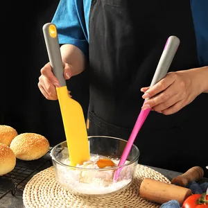Large yellow and pink silicone baking spatulas used in a kitchen setting to mix ingredients