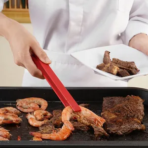 Rote hitzebeständige Silikon-Küchenzange, die gegrillte Garnelen vom Grillrost hebt