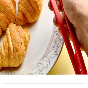 Close-up of red non-slip silicone food tongs picking up a croissant on a plate